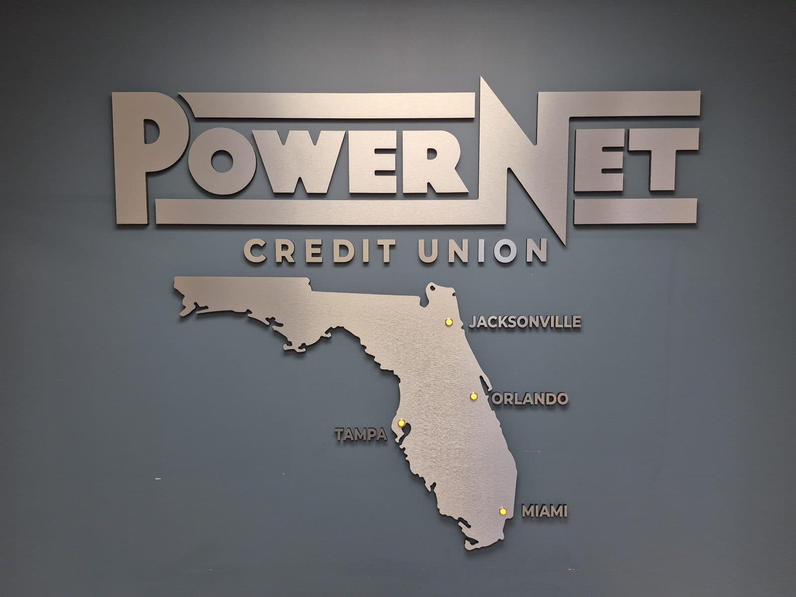 Brushed metal-finish PowerNet Credit Union lobby sign with a cut Florida map and lit location markers