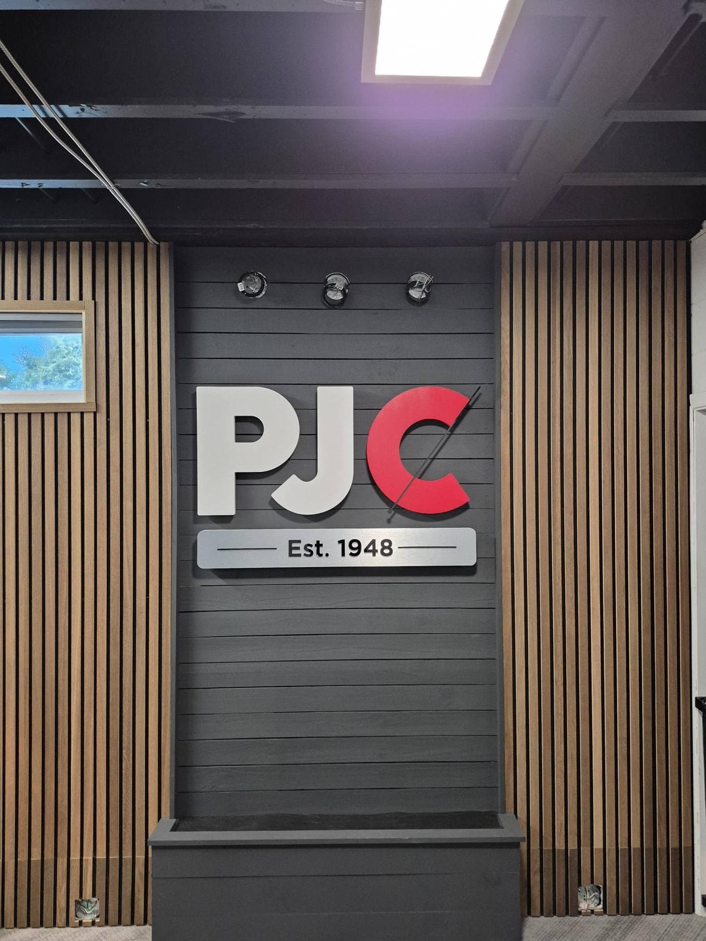 PJC dimensional lobby letters in white and red with a brushed plaque on a dark shiplap and wood slat wall